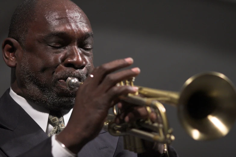 a man in suit playing a trumpet while standing with his eyes closed