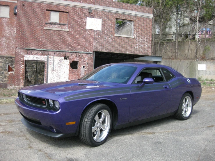 a purple dodge charger car parked in front of an abandoned warehouse