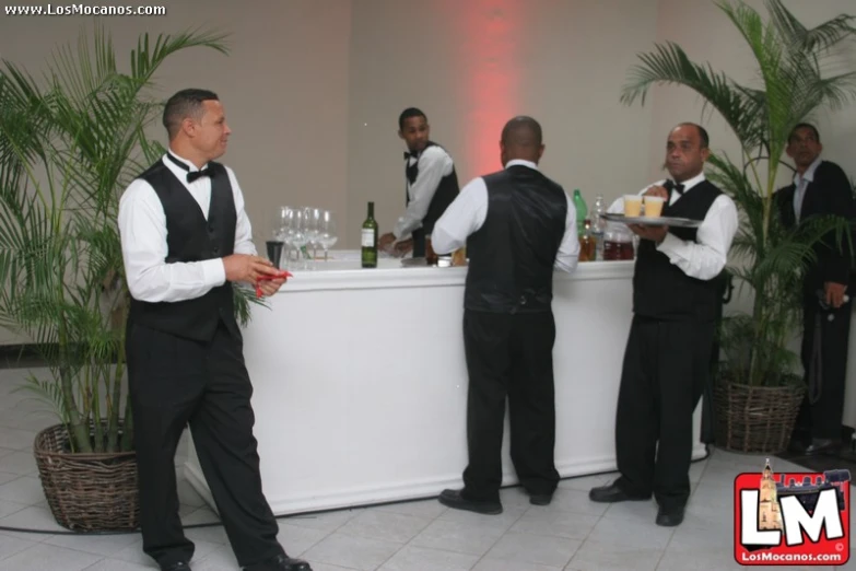 four men dressed in black suits and bow ties are standing at a bar