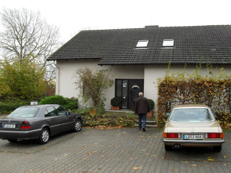 a man walking in front of a house, while his car is parked in front