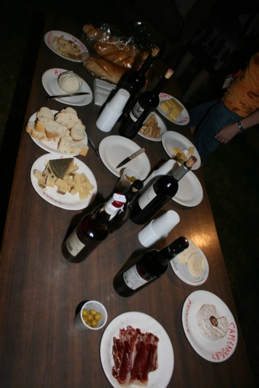 a table full of assorted cheeses, wines and bread