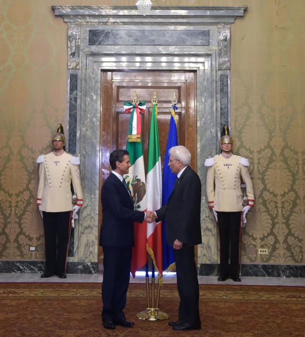 two men shake hands near flags in a room