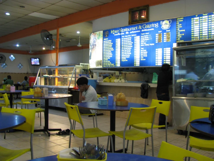 a restaurant with a menu board and blue and yellow chairs