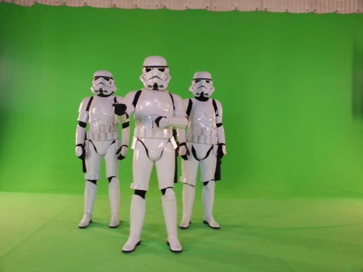 three white figurines dressed as stormtroopers are standing in front of a green screen