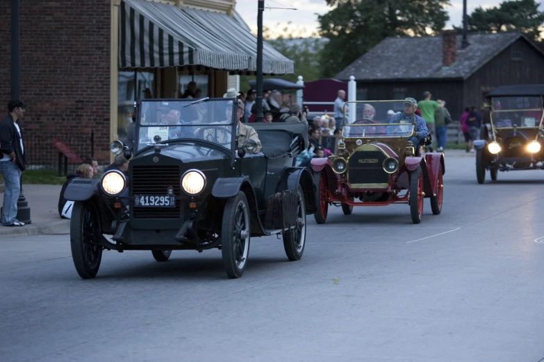 a group of people in old fashioned cars traveling on a road