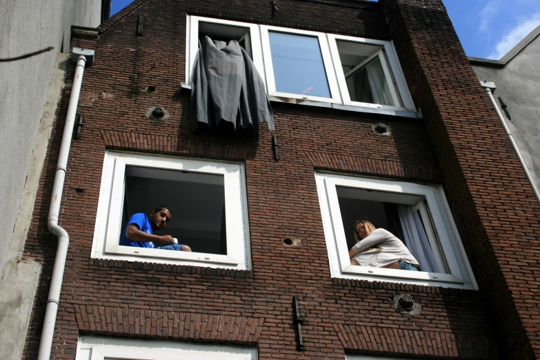 two men sit on the windows of a brick building