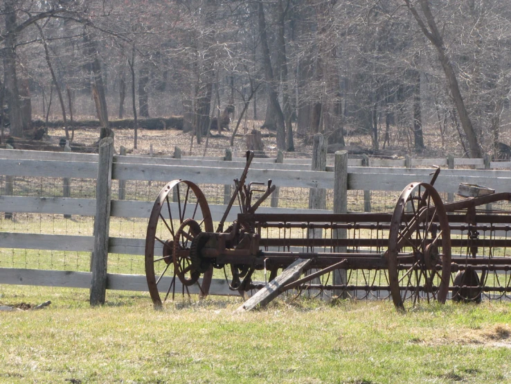 a set of old farm implements resting in the grass beside a fence