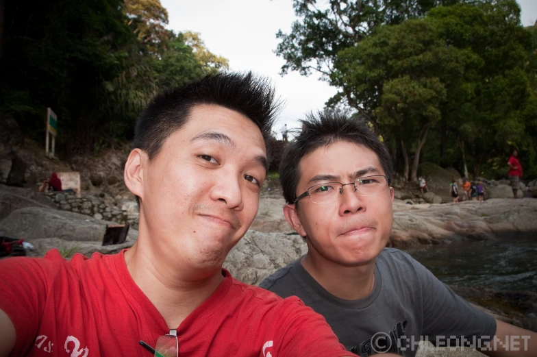two asian men are taking a selfie near a body of water