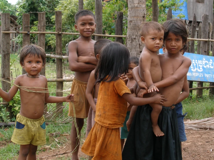 six children standing around in front of a wooden fence