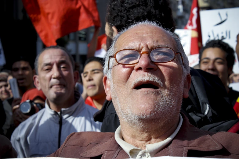 man with glasses making a face as others gather behind him