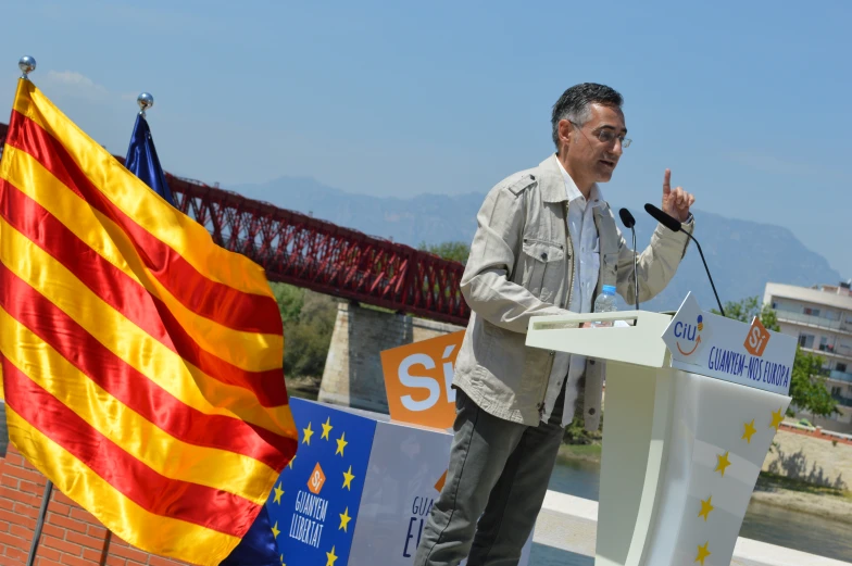 the man is speaking from a podium by a flag