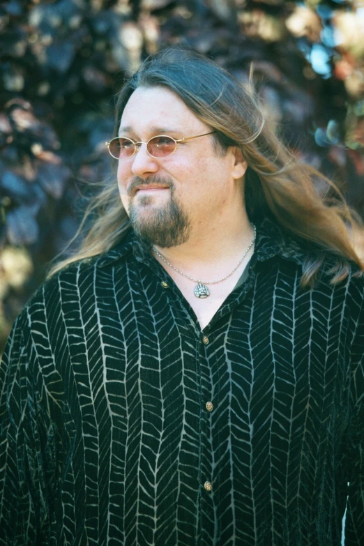 a man wearing a shirt and sunglasses poses in front of a tree