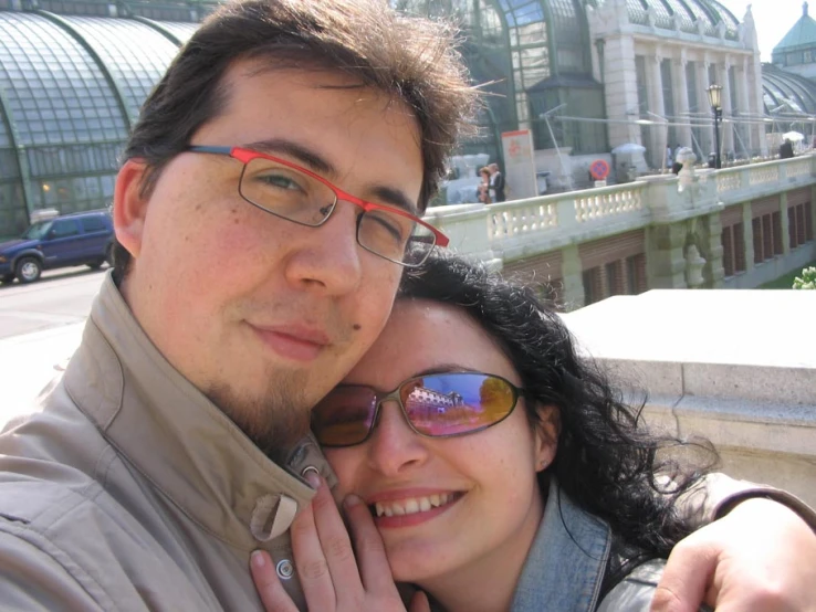 two people pose for a selfie in front of some buildings