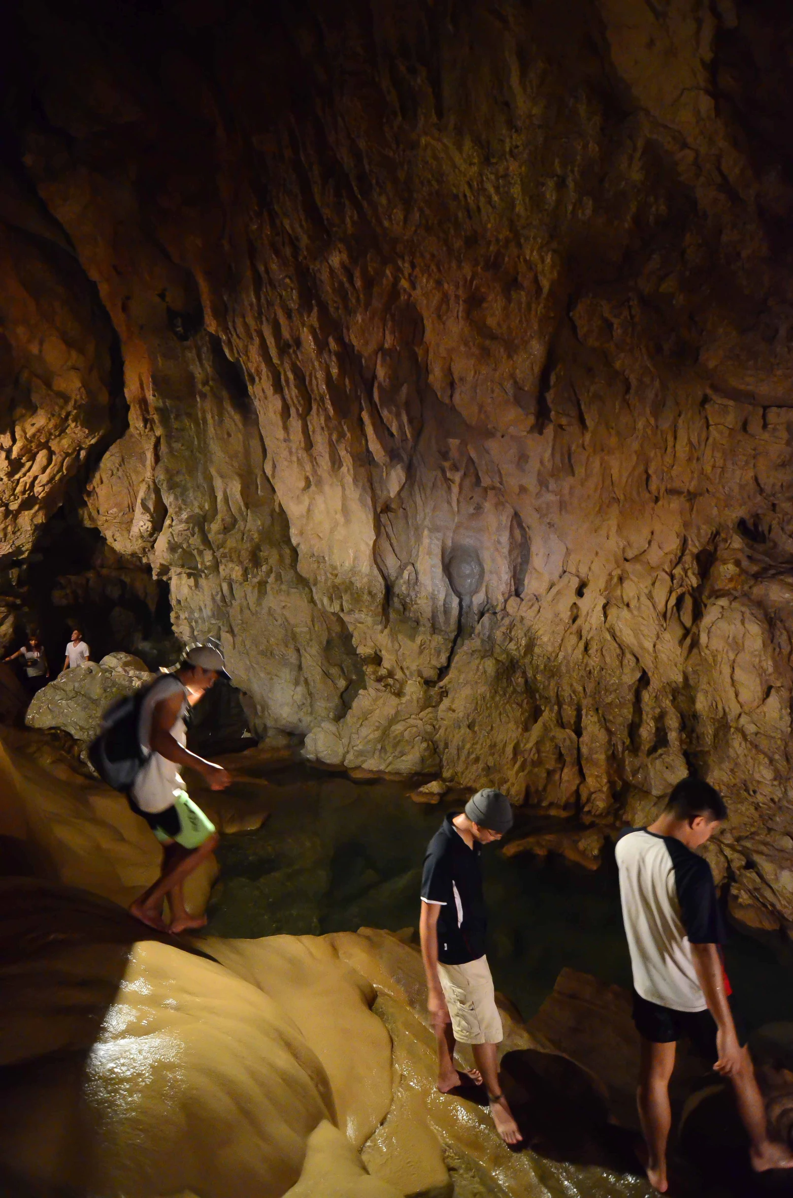 two young men exploring the cave, one is in a green hat and the other is looking down