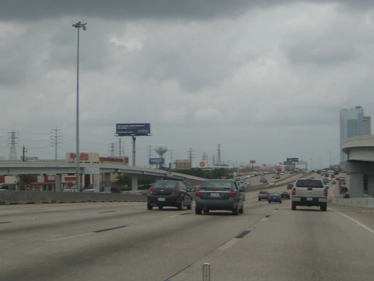 cars on a road with stormy skies and signs in the background