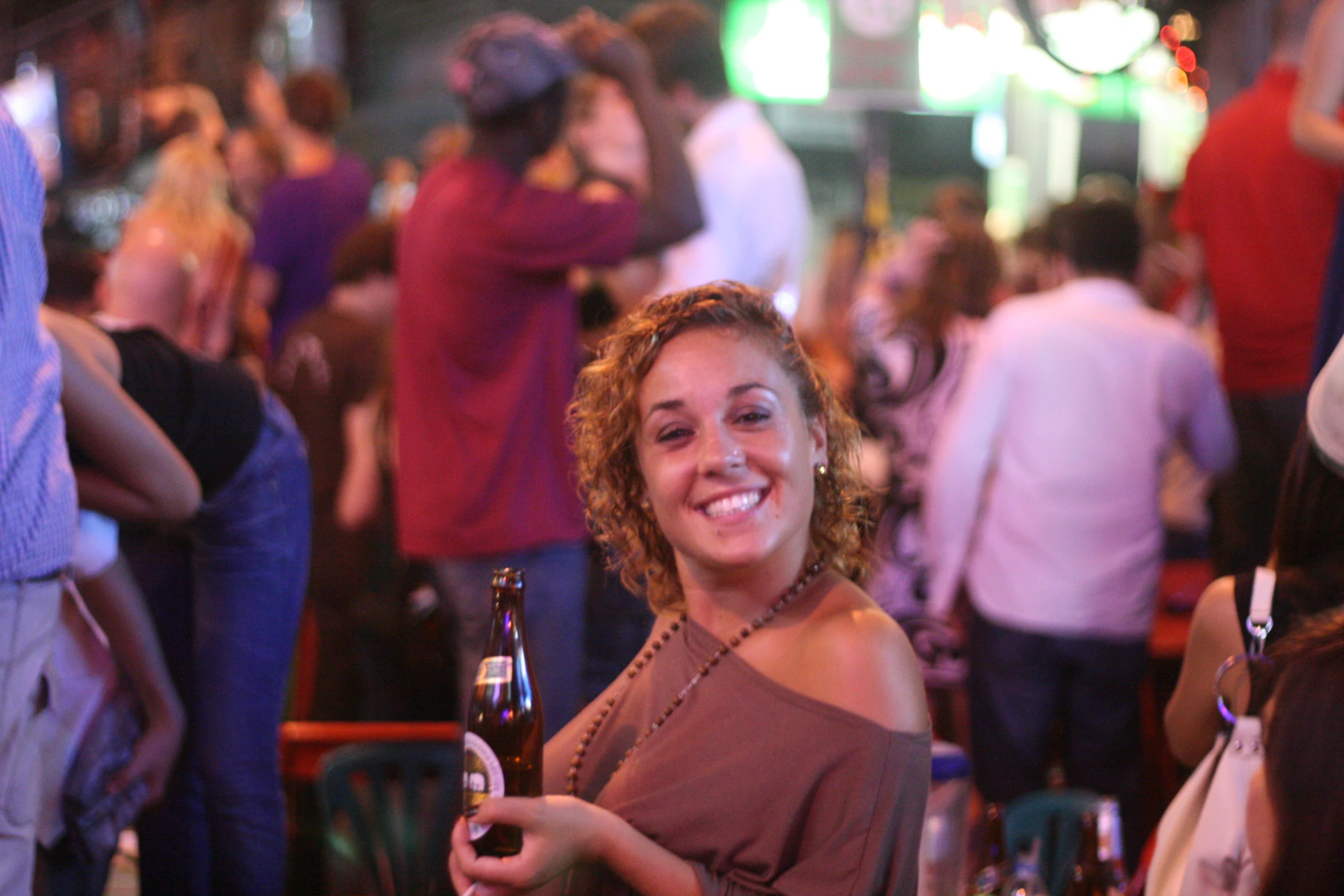 there is a woman smiling holding a beer at a bar