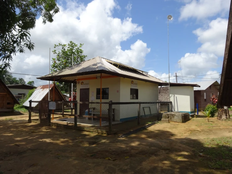 a small building with a metal fence on a field near a tree