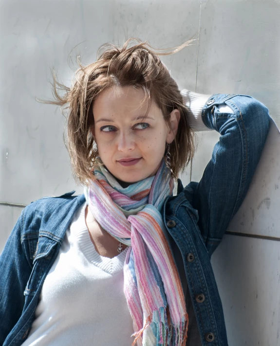 a woman wearing a scarf stands against a wall