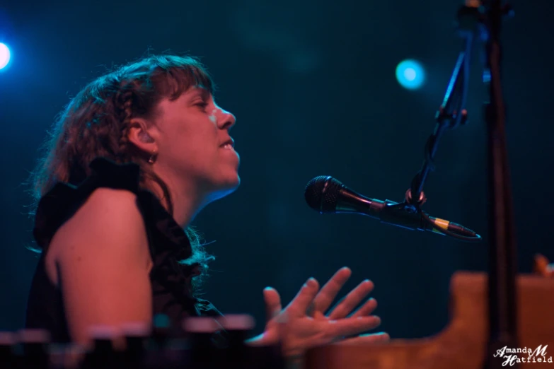 a woman with brown hair and black dress on stage, with a microphone