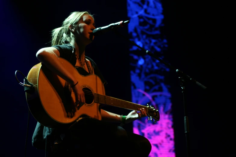 a woman playing guitar on stage with a microphone in front of her