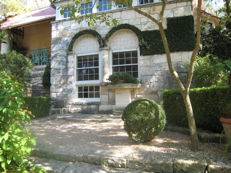 a house is shown from the backyard with hedges and potted plants