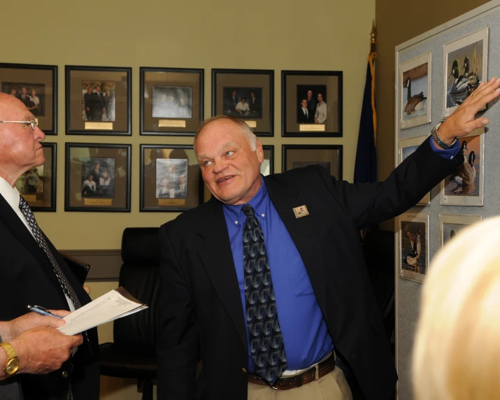 two men in suits standing in front of framed pictures