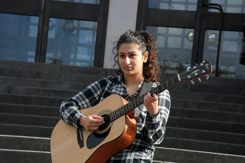 the girl in the plaid shirt is playing a guitar