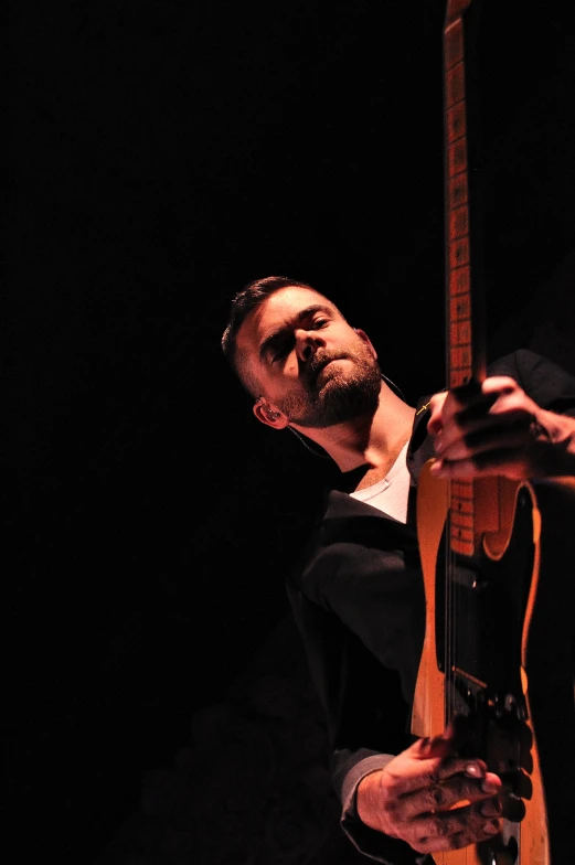 a man plays a guitar against a dark backdrop