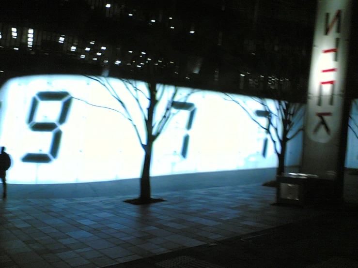 the clock is projected on the wall behind a lone tree