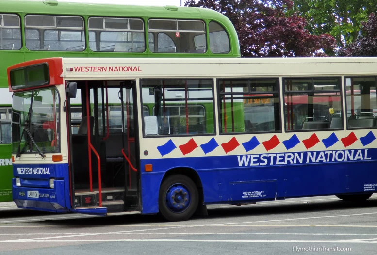 the green, blue, and white bus is stopped at the curb