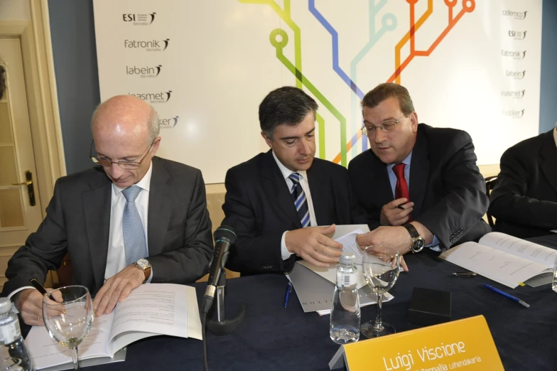 three men in business attire sitting at a table with book and glasses