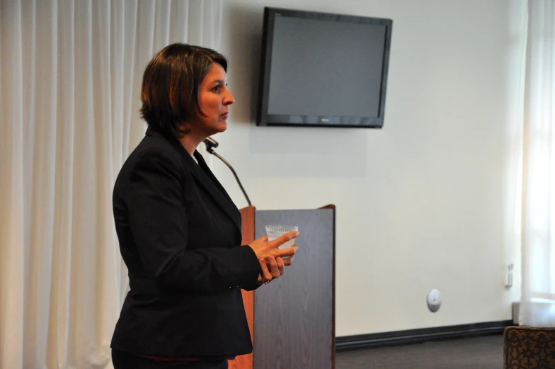 a woman speaking from a podium in front of a tv