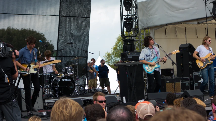 four band members performing on stage in front of a crowd