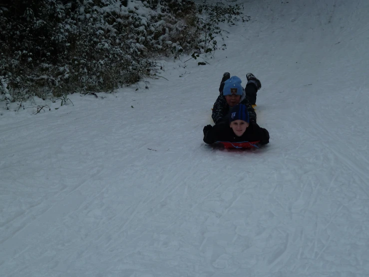 two s riding sleds down a snowy hill