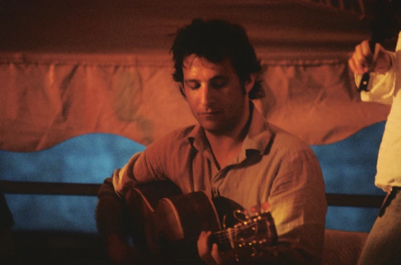 a man sitting and playing a guitar in front of another person