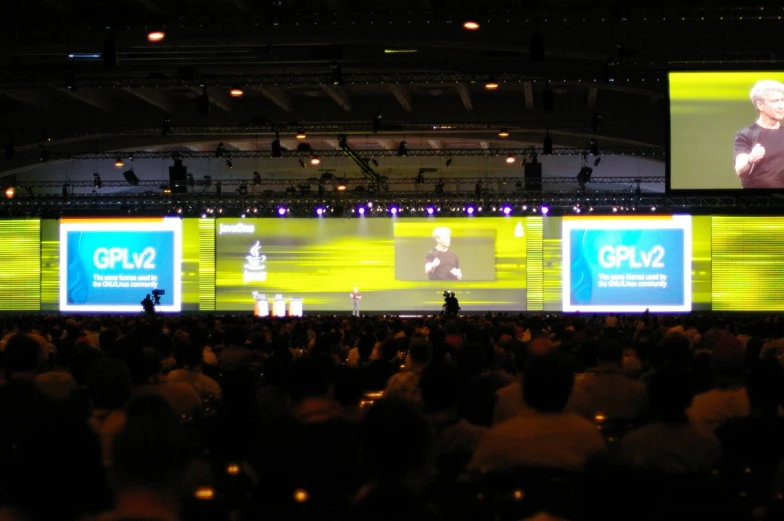 an audience looking at three large video screens with someone talking on them