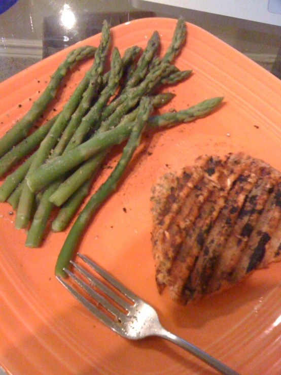 meat and asparagus on an orange plate with a fork