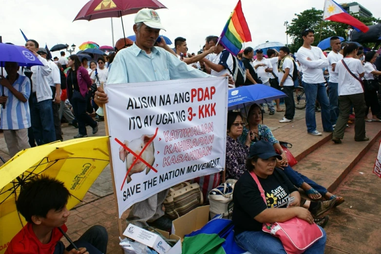 many people holding protest signs and umbrellas on a sidewalk