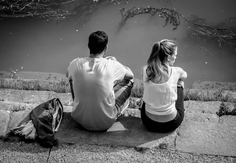 the two people are sitting on a bench next to a lake