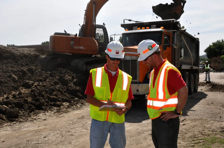 two men in bright vests standing next to a large truck