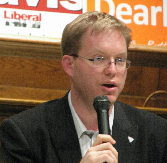 a man speaking with a microphone in front of a large sign