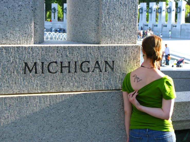 a woman stands next to the wall in front of the michigan monument