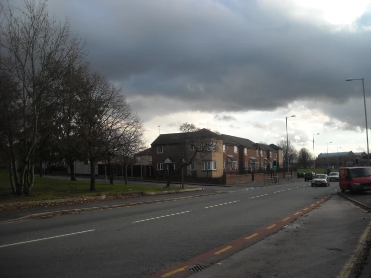 a dark and cloudy sky over a neighborhood with several vehicles parked on the side