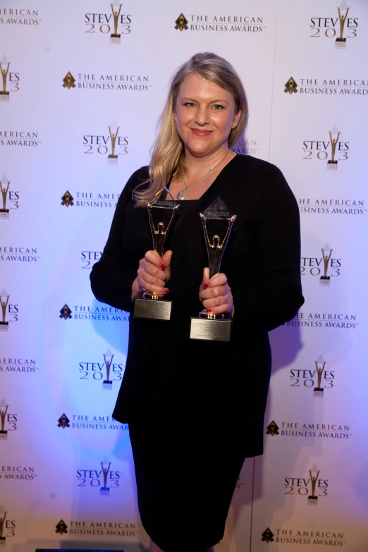 a woman is posing holding some trophies in her hands