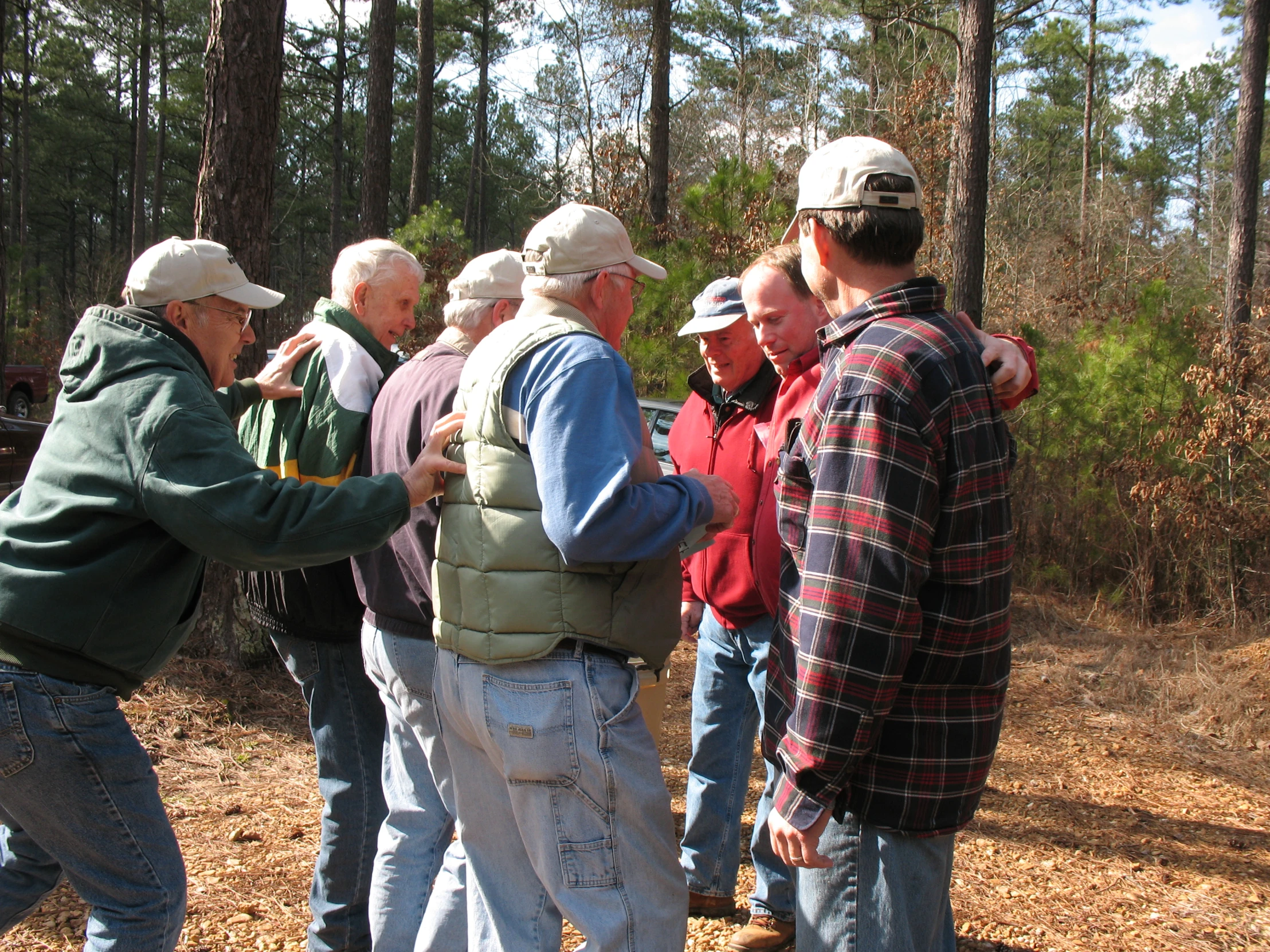 group of men stand in a forest looking at soing