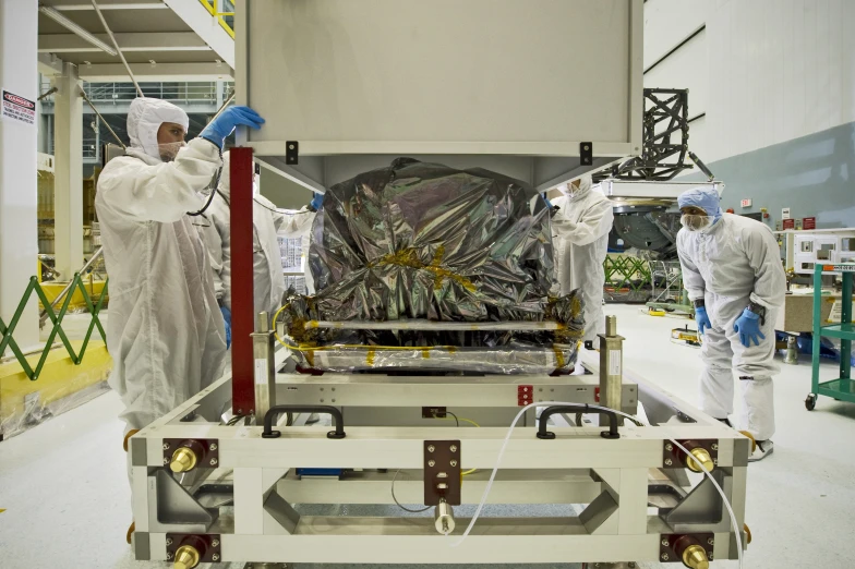 three people in white suits stand around an assembly line