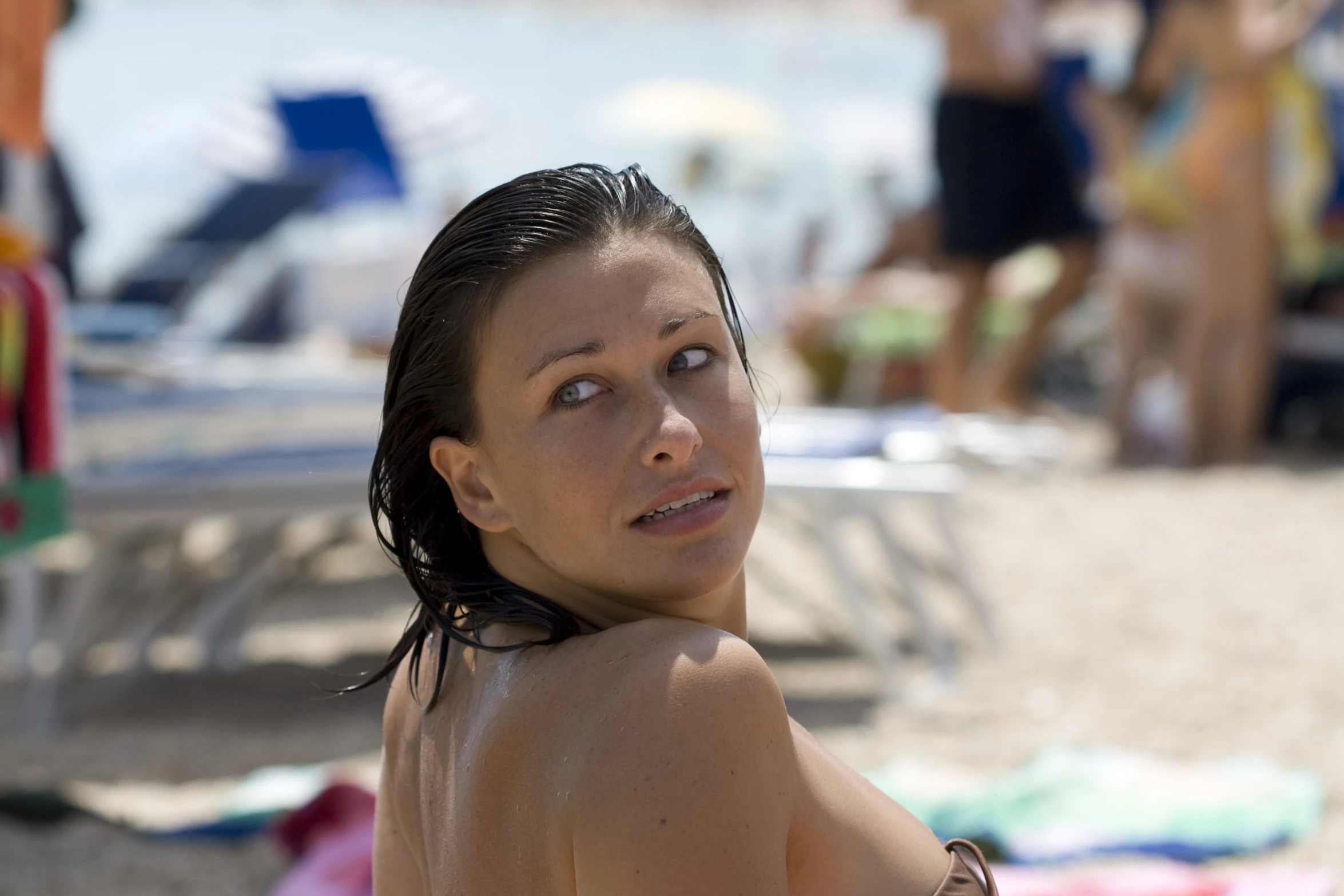 a woman sitting down on the beach in her bikini