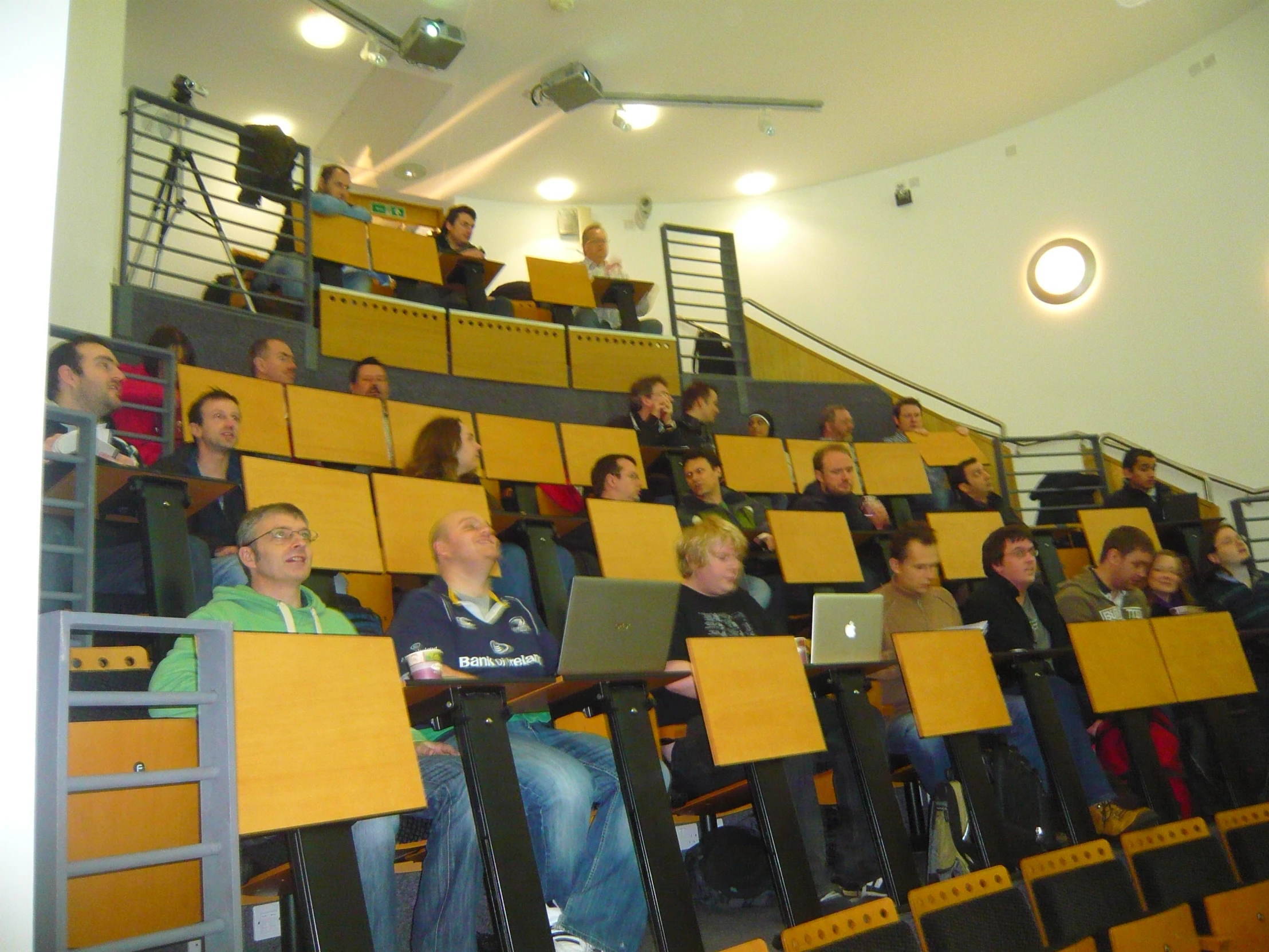 a group of people sitting in a auditorium full of yellow chairs