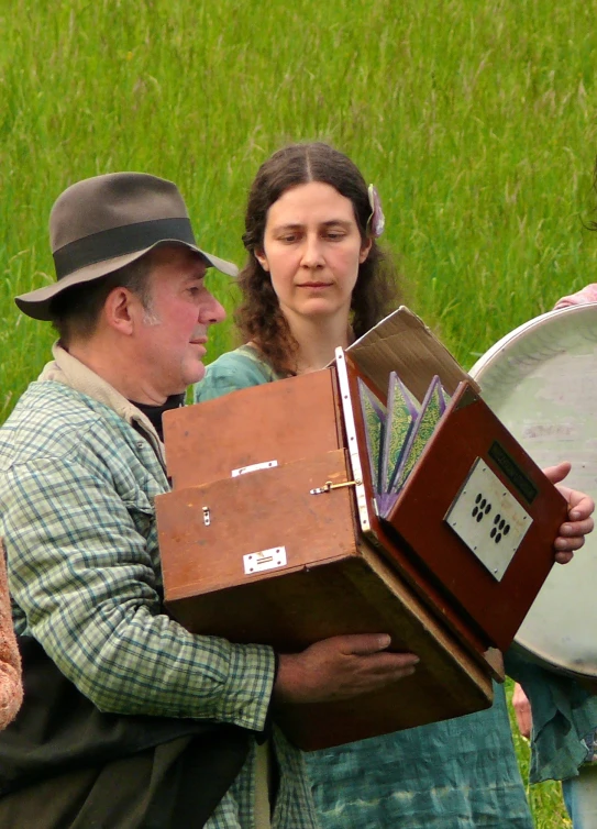 a woman holding two wooden boxes with tags on them and one man behind her