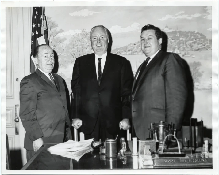 three men in suits pose for a picture with a flag behind them